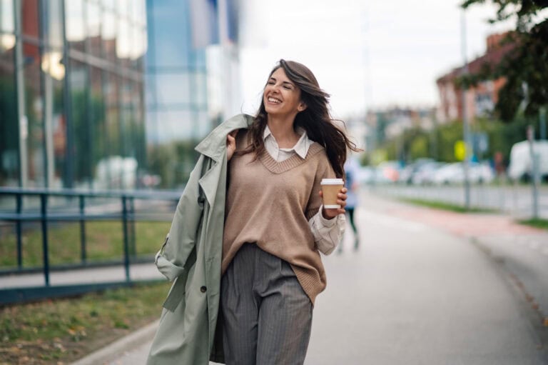 Fröhliche Frau mit Kaffee auf der Straße, urbanes Umfeld, positive Stimmung.