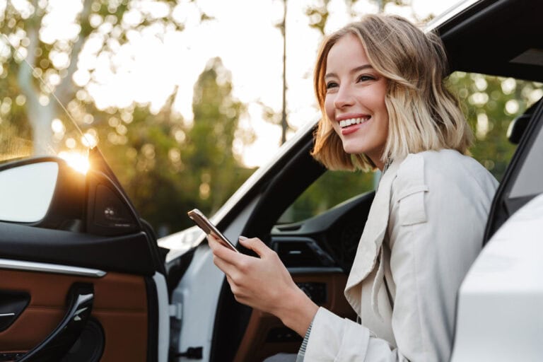 Glückliche Frau im Auto nutzt Smartphone bei Sonnenuntergang.